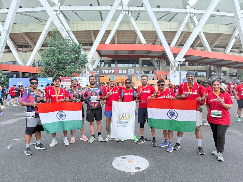 दिल्ली के जवाहरलाल नेहरू स्टेडियम में टफमैन हाफ मैराथन के दौरान राष्ट्रीय ध्वज और पूर्णिया रन क्लब के बैनर के साथ पदक दिखाते धावक।